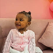 Ely joined the competition — help win amazing prizes! toddler, child, smile, pink_cardiagn, white_dress, curly_hair, earrings, couch, pillow, indoor, happy, cute, fashion, portrait, sitting, baby, cozy, soft_lighting, background, home