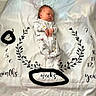 age_tracker, baby, baby_clothing, black_text, cute, indoors, infant, lying_down, milestone_blanket, months, newborn, onesie, peaceful, portrait, resting, sleeping, soft_lighting, weeks, white_blanket, years