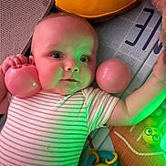 Oliver is registered to the contest to win money with this photo: baby, infant, play_mat, ball, pink_ball, onesie, striped_onesie, toys, rattle, pillow, plush_toy, mesh_side, green_light, close_up, face, eyes, hand, indoor, playtime, portrait