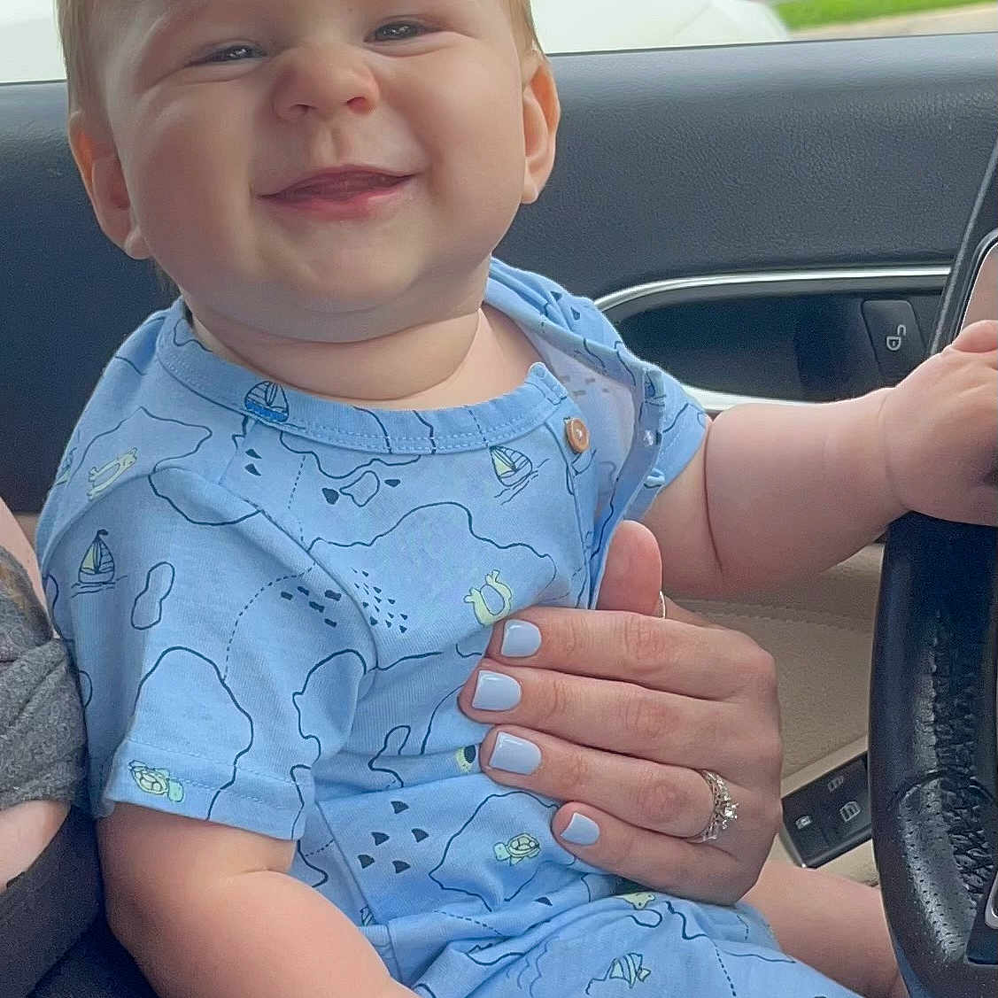 James is registered to the contest to win money with this photo: baby, car, clothing, dress, face, happy, head, laughing, machine, person, photography, portrait, sedan, sitting, smile, suv, t_shirt, transportation, vehicle, wheel