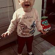 Lola participe au concours pour gagner de l'argent avec cette photo : toddler, child, laughing, standing, indoors, sweatshirt, angel_and_stitch, toy_car, floor, tile_floor, smile, person, clothing, happy, home, furniture, cabinet, socks, shoes, hair_tied