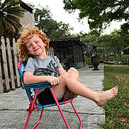 Angel joined the competition — help win amazing prizes! backyard, barefoot, casual, chair, child, concrete, curly_hair, daylight, fence, grass, happy, outdoor, person, playful, red_hair, relaxed, shorts, smiling, trees, tshirt