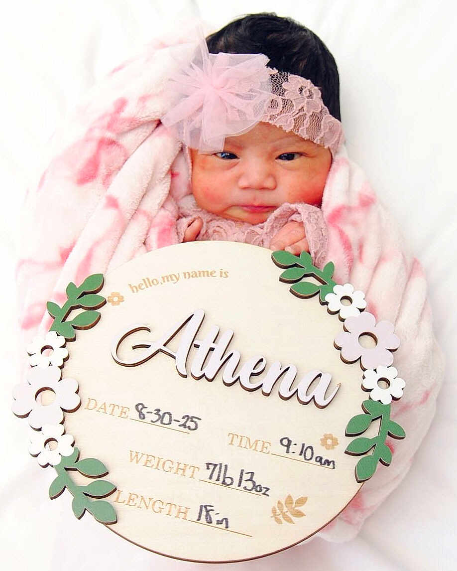 Athena is registered to the contest to win money with this photo: newborn, baby, infant, blanket, headband, portrait, cute, sleeping, soft, pink, name_sign, wooden_sign, flower_decoration, announcement, wrapped, child, face, small_hands, lying_down, indoors