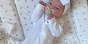 Millie Mae is registered to the contest to win money with this photo: baby, infant, onesie, white_clothing, headband, bow, pacifier, star_pattern, padded_surface, lying_down, newborn, cute, sleepy, child, soft_texture, fabric, indoors, peaceful, small_hands, face