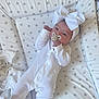 baby, infant, onesie, white_clothing, headband, bow, pacifier, star_pattern, padded_surface, lying_down, newborn, cute, sleepy, child, soft_texture, fabric, indoors, peaceful, small_hands, face
