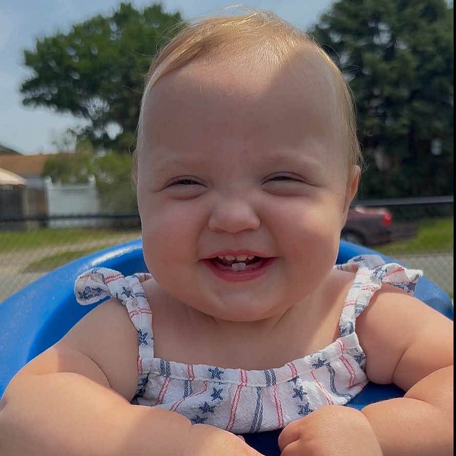 Scarlett is registered to the contest to win money with this photo: baby, blue_seat, child, cute, dress, face, fence, grass, hand, happy, infant, nature, outdoor, person, portrait, skin, smiling, summer, sunlight, trees