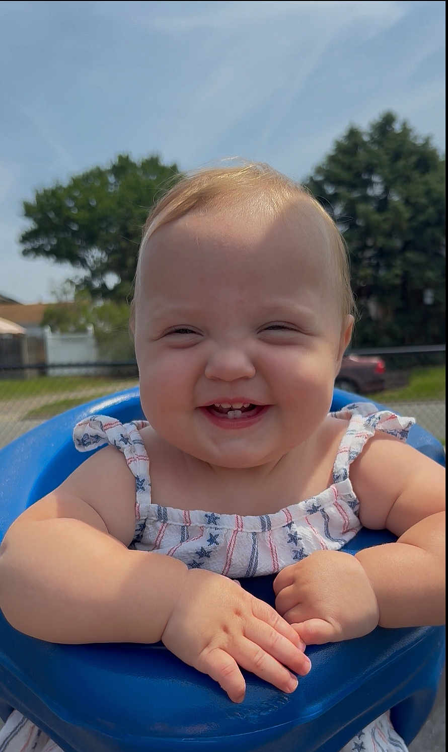 Scarlett is registered to the contest to win money with this photo: baby, child, smiling, outdoor, blue_seat, dress, sunlight, hand, face, happy, cute, infant, person, summer, nature, trees, fence, grass, skin, portrait