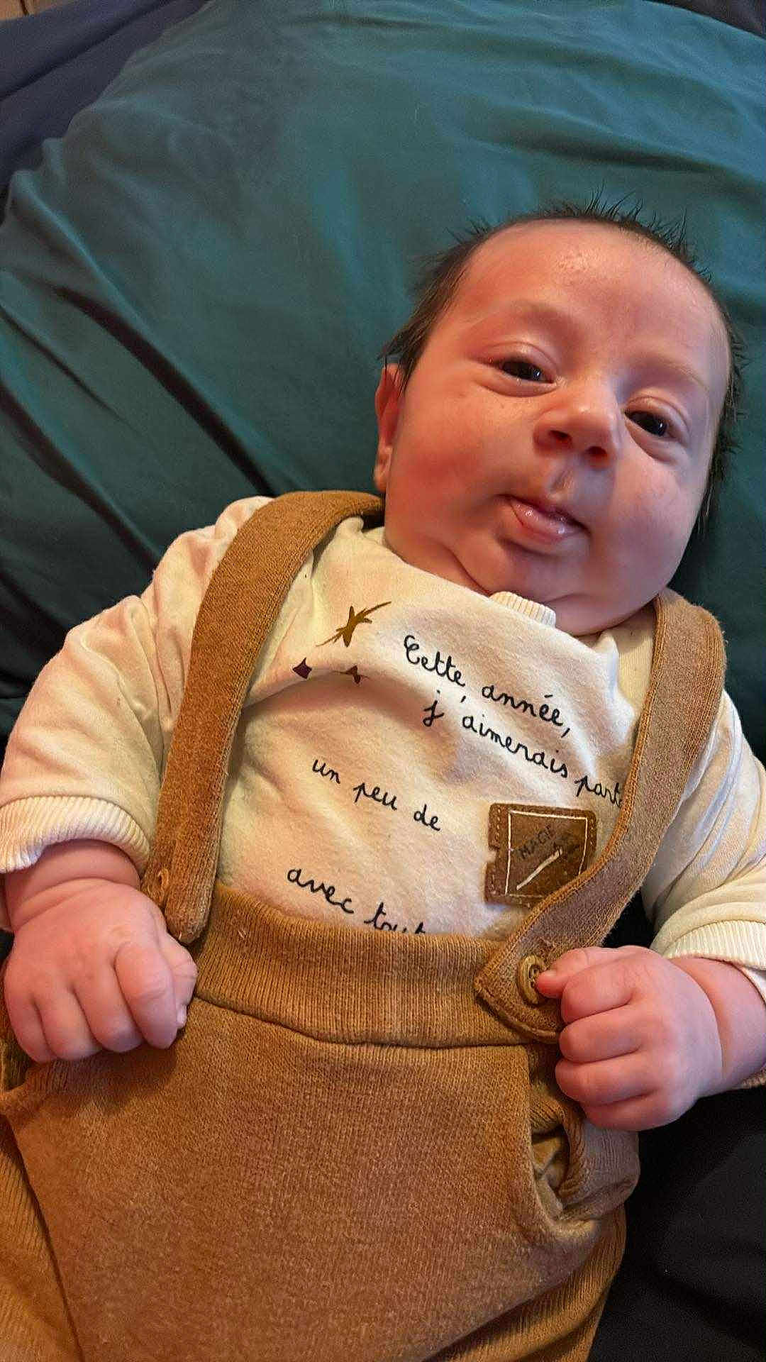 Malo participe au concours pour gagner de l'argent avec cette photo : baby, infant, child, face, hand, clothing, overalls, shirt, text, expression, lying_down, indoor, skin, cute, young, person, baby_fashion, warm_colors, soft_texture, closeup