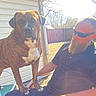 Aries is registered to the contest to win money with this photo: dog, man, beard, sunglasses, outdoor, sunlight, chair, fence, patio, casual, relaxing, pet, animal, brindle, human, backyard, daylight, shadow, clothing, resting