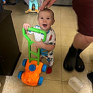 Lamichael is registered to the contest to win money with this photo: toddler, child, toy, lawnmower, indoor, floor, pajamas, smile, hand, playful, dinosaur_rocker, background, furniture, happy, person, footwear, plastic_container, home, carpet, room