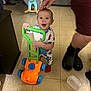 toddler, child, toy, lawnmower, indoor, floor, pajamas, smile, hand, playful, dinosaur_rocker, background, furniture, happy, person, footwear, plastic_container, home, carpet, room