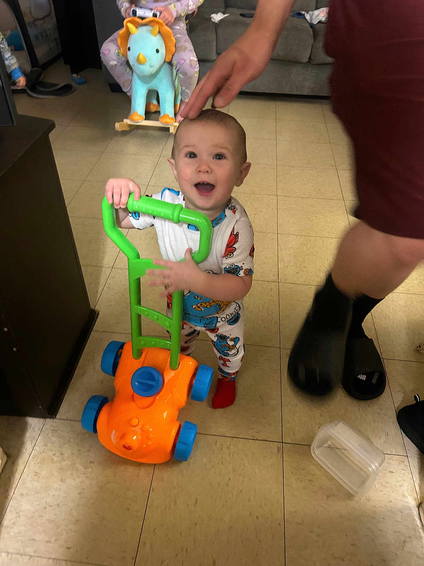 Lamichael is registered to the contest to win money with this photo: toddler, child, toy, lawnmower, indoor, floor, pajamas, smile, hand, playful, dinosaur_rocker, background, furniture, happy, person, footwear, plastic_container, home, carpet, room