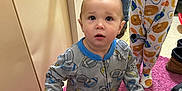 Lamichael is registered to the contest to win money with this photo: adult, breakfast_pattern, carpet, child, clothing, curious, cute, expression, floor, football_pattern, footwear, home, indoor, legs, pajamas, person, pink_rug, shoes, standing, toddler