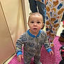 adult, breakfast_pattern, carpet, child, clothing, curious, cute, expression, floor, football_pattern, footwear, home, indoor, legs, pajamas, person, pink_rug, shoes, standing, toddler
