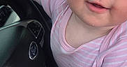 Coriann is registered to the contest to win money with this photo: baby, car, child, close_up, dashboard, driver, greenery, happy, indoor, infant, photograph, pink_clothing, portrait, short_sleeves, sitting, smiling, steering_wheel, striped_shirt, vehicle, window