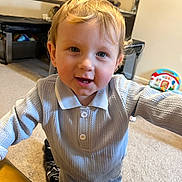 Marley is registered to the contest to win money with this photo: baby, blonde_hair, blue_eyes, carpet, casual, child, clothing, cute, happy, home, indoor, knitwear, living_room, person, portrait, smiling, table, toddler, toy, young_child