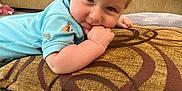 Marley is registered to the contest to win money with this photo: baby, blue_clothing, carpet, child, curly_hair, cushion, cute, face, floor, furniture, hand, home, indoor, light_hair, pattern, person, relaxed, smiling, sofa, toddler