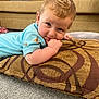 Marley is registered to the contest to win money with this photo: baby, child, cushion, carpet, sofa, furniture, indoor, person, face, hand, blue_clothing, pattern, curly_hair, light_hair, smiling, cute, toddler, floor, relaxed, home