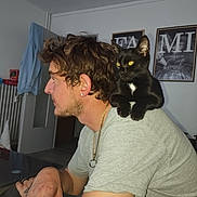 Shadow participe au concours pour gagner de l'argent avec cette photo : black_cat, casual_clothing, cat, curly_hair, domestic_animal, earring, furniture, gold_chain, home_interior, indoor, looking_away, man, pet, portrait, relaxed, seated, shoulder_perch, table, tattoo, wall_art