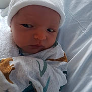 Kasson joined the competition — help win amazing prizes! baby, newborn, infant, hat, blanket, clothing, dinosaur_pattern, onesie, bed, hospital, wrapped, face, expression, person, cute, sleepwear, soft, cozy, indoors, portrait