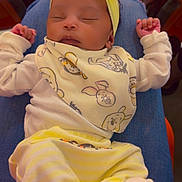 Love is registered to the contest to win money with this photo: baby, sleeping, headband, bib, yellow_clothing, striped_pants, socks, person, lap, indoor, orange_chairs, cute, peaceful, child, infant, clothing, relaxing, resting, portrait, closeup