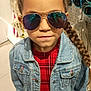 child, girl, sunglasses, denim_jacket, plaid_dress, braided_hair, indoor, retail_store, fashion, clothing, accessories, shopping, portrait, person, casual_wear, reflection, standing, hair_style, cool, style