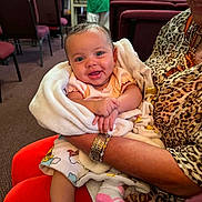 Aviana is registered to the contest to win money with this photo: baby, infant, blanket, smile, person, arm, clothing, jewelry, leopard_print, socks, indoor, chair, carpet, people, background, holding, cute, happy, toddler, portrait