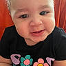 baby, child, smiling, face, person, cute, toddler, black_shirt, colorful, flower_print, indoors, orange_background, happy, portrait, close_up, skin, eyelashes, cheeks, head, expression