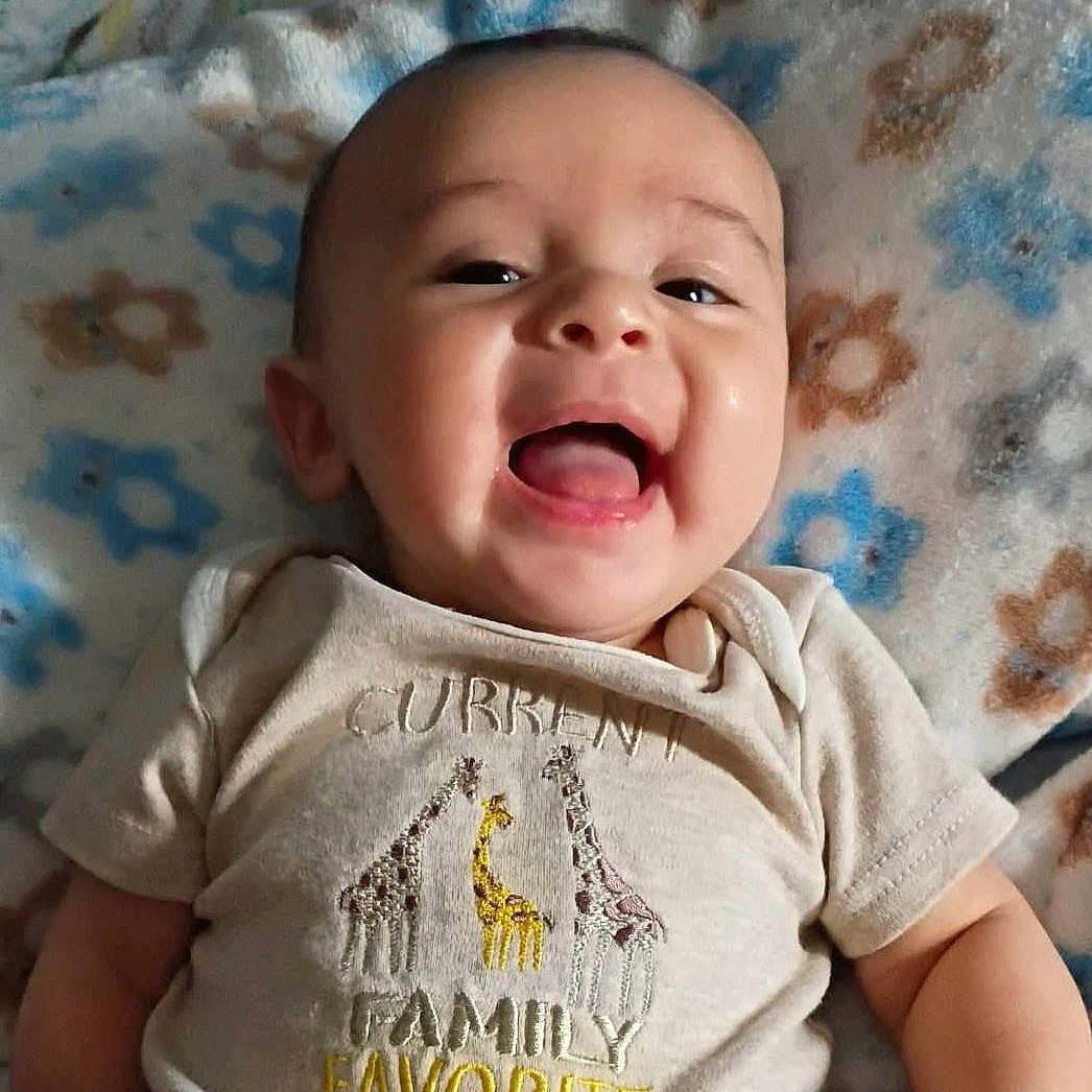 Osias joined the competition — help win amazing prizes! baby, smiling, infant, face, clothing, shirt, giraffe, text, blanket, pattern, happy, tongue, cute, child, portrait, lying_down, closeup, skin, person, indoors