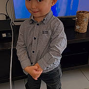 Kënzo participe au concours pour gagner de l'argent avec cette photo : child, toddler, barefoot, smiling, indoor, floor, toy, superman, television, shirt, pants, hair, face, person, hands, clothing, tile_floor, cabinet, decor, playful