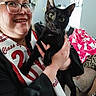 animal, black_cat, blanket, cat, celebration, face, furniture, glasses, graduation_cap, graduation_gown, hand, happy, home, indoor, living_room, person, pet, sash, smile, window