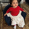 armchair, baby, blanket, child, coffee_table, cozy, curly_hair, earring, happy, home_interior, living_room, playful, portrait, red_sweater, rug, seated, smile, sock, table, toddler