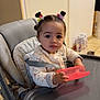 child, toddler, baby, high_chair, silicone_plate, pink_plate, hair_buns, hair_clips, big_eyes, strapped_in, patterned_clothing, seat_cushion, indoor, kitchen, tiled_floor, door, diaper_pack, curious_expression, hand_holding, portrait