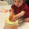 birthday_cake, cake, celebration, child, close_up, curious_expression, curly_hair, decorations, dessert, fondant, hands, icing, indoor, portrait, red_dress, sprinkles, sweet, table, toddler, toy_deer