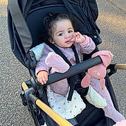 Julia participe au concours pour gagner de l'argent avec cette photo : baby, blanket, child, curly_hair, hand, handlebar, harness, hood, outdoor, pavement, pink_clothing, plush_toy, portrait, pram, seat_belt, sitting, stroller, toddler, toy, wheel