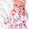 Aria is registered to the contest to win money with this photo: baby, infant, child, portrait, floral_outfit, pink_clothing, headwrap, pacifier, smiling, blue_eyes, lying_down, blanket, white_background, soft_texture, indoor, closeup, fashion, adorable, hand, baby_photography