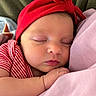 newborn, baby, sleeping, infant, portrait, close_up, face, red_headband, striped_clothing, pink_blanket, cuddling, peaceful, indoors, soft_lighting, relaxed, resting, parent, arm, cozy, photography
