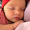 baby, sleeping, newborn, infant, portrait, face, red_hat, knotted_hat, pink_blanket, blanket, clothing, resting, peaceful, indoors, close_up, soft_lighting, hands, closed_eyes, smartphone_screenshot, messaging_interface