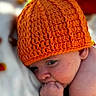 baby, infant, child, portrait, orange_hat, crocheted_hat, blanket, lying_down, face, eyes, hand, fist, smiling, cozy, indoor, close_up, textile, colorful, sleeping_area, photography