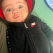 Jeremiah is registered to the contest to win money with this photo: baby, hoodie, nike, black_clothing, red_hood, blue_blanket, green_background, infant, face, eyes, expression, zipper, casual_wear, indoors, child, portrait, young_child, clothing, person, cute
