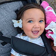 Serenity joined the competition — help win amazing prizes! baby, child, smiling, happy, portrait, stroller, flower, stuffed_animal, pink_toy, outdoor, sitting, infant, face, eyes, open_mouth, brown_hair, clothing, blanket, harness, garden