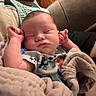 baby, blanket, sleeping, couch, wooden_wall, infant, person, cozy, indoor, comfort, soft, rest, peaceful, child, clothing, relaxation, home, nap, furniture, portrait