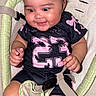 baby, child, smiling, curly_hair, black_clothing, pink_number, baby_seat, straps, happy, cute, chubby_cheeks, infant, indoor, person, young_child, sitting, closeup, portrait, playful, comfortable