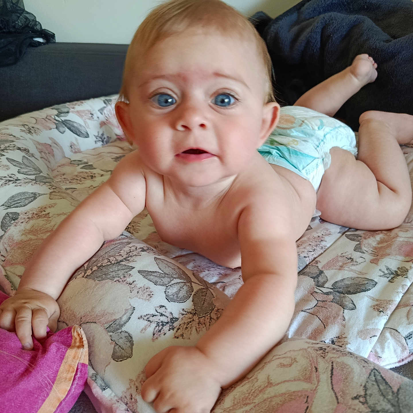 Elyana participe au concours pour gagner de l'argent avec cette photo : baby, blue_eyes, child, curious, cushion, diaper, floral_pattern, hand, indoor, infant, laying, light_skin, looking, person, plush, reaching, soft_furniture, toddler, upclose, young