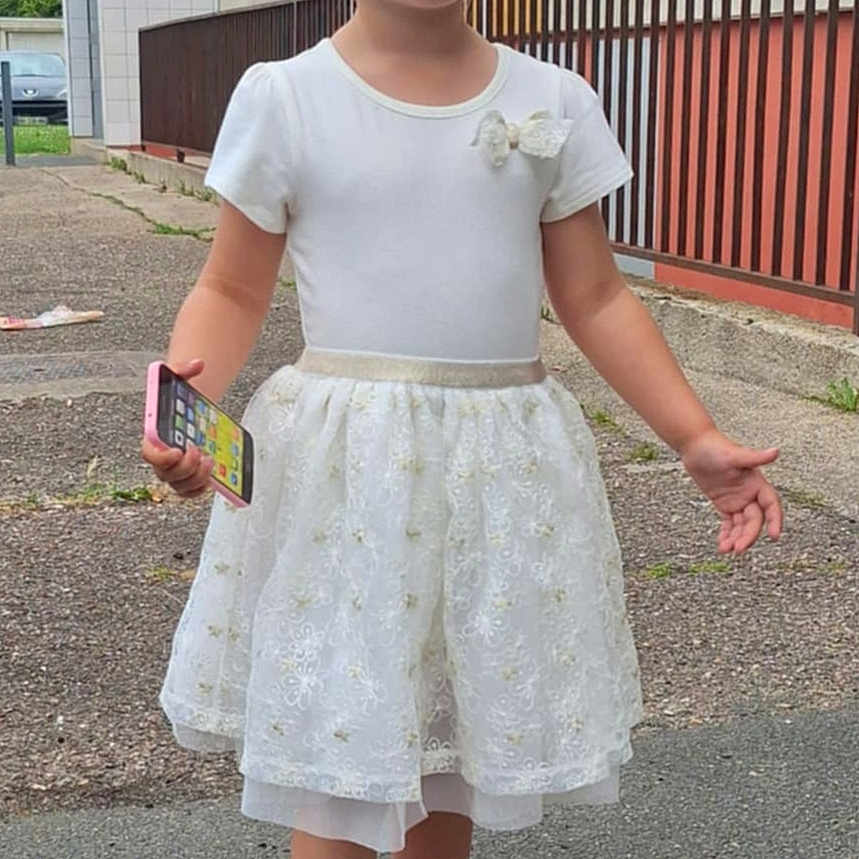 Emily a rejoint le concours — aidez-le/la à gagner de superbes lots ! blonde_hair, building, casual_pose, child, daytime, fence, footwear, girl, hello_kitty, holding, outdoor, person, pink_shoes, short_sleeves, sidewalk, smartphone, smile, summer, urban, white_dress
