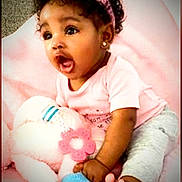 Liliana joined the competition — help win amazing prizes! baby, child, curly_hair, pink_headband, pink_shirt, gray_pants, plush_toy, blanket, sitting, barefoot, earrings, happy, cute, indoor, infant, expression, soft_toy, pink, playful, portrait