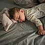 baby, sleeping, toddler, bed, blanket, pajamas, floral_print, hand, face, cozy, child, indoors, soft_lighting, rest, peaceful, cute, curly_hair, comfort, nap_time, serene