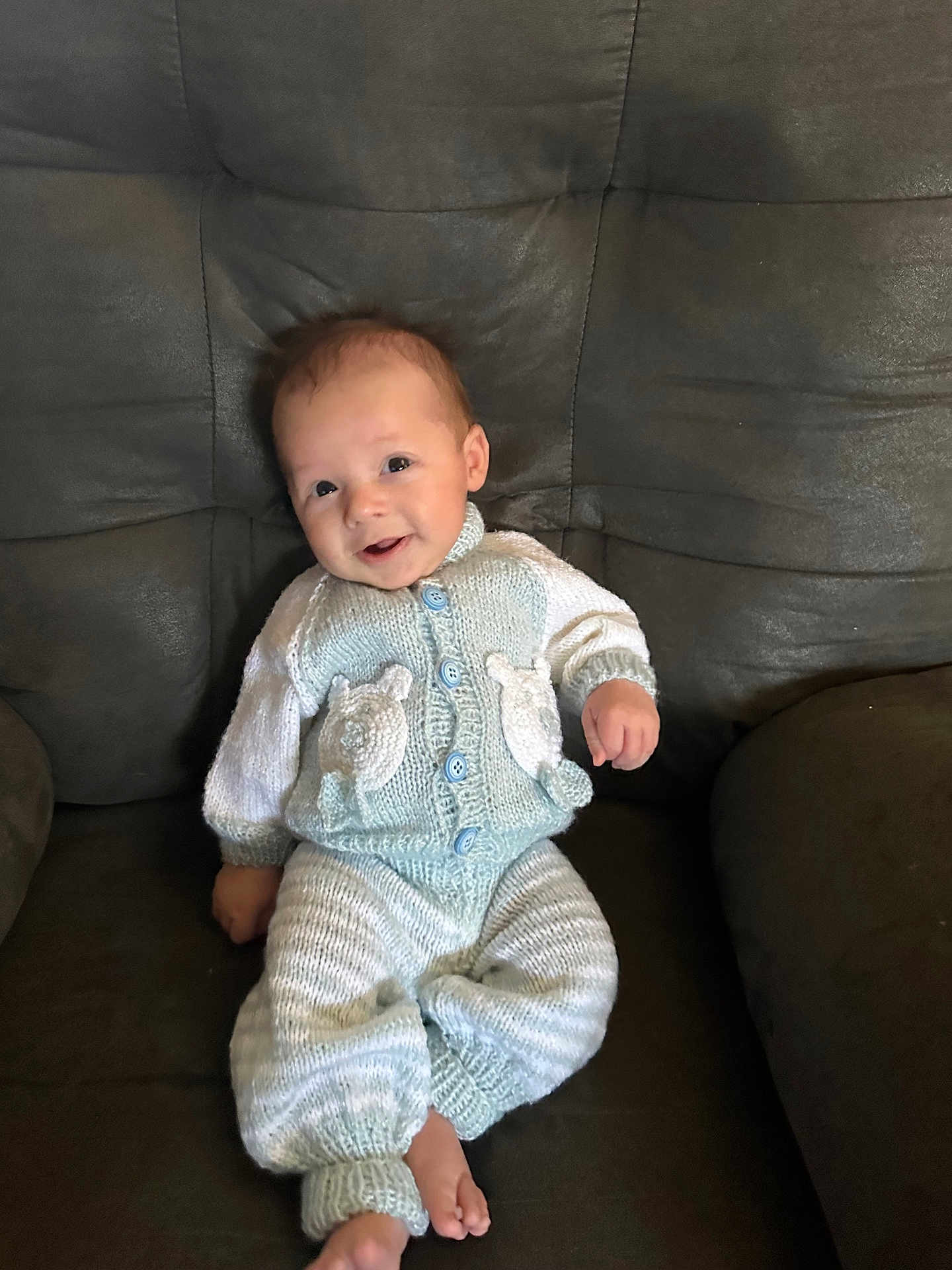 Sy Mir is registered to the contest to win money with this photo: baby, infant, child, knitted_clothing, sitting, smiling, face, head, couch, chair, cozy, cute, comfort, indoor, portrait, young, happy, feet, buttoned_sweater, casual