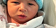 Sy Mir joined the competition — help win amazing prizes! baby, newborn, face, hat, blanket, wrapped, infant, close_up, cute, soft_lighting, indoors, portrait, sleepwear, knit, warm, child, expression, skin, headwear, cozy