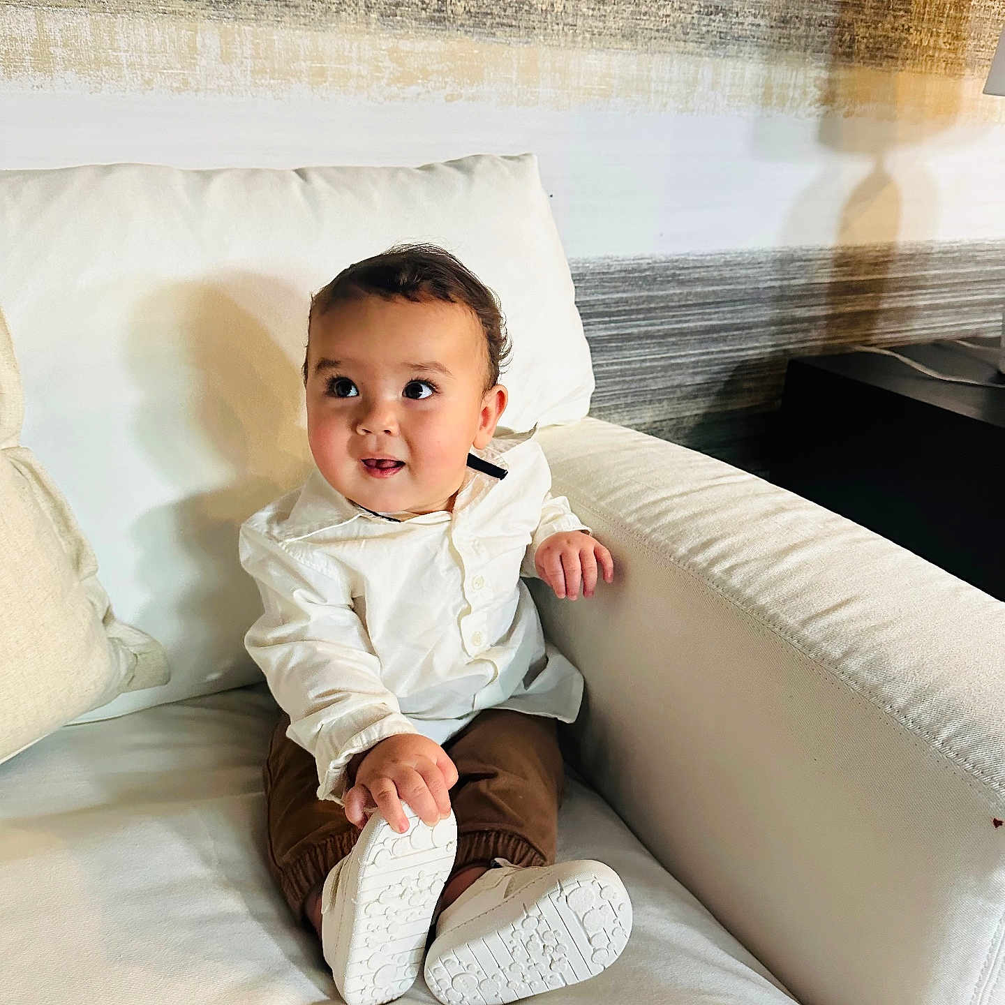 Mathius Durán joined the competition — help win amazing prizes! baby, brown_pants, child, comfortable, couch, cozy, curious_expression, cute, furniture, home, indoor, living_room, person, portrait, sitting, smiling, toddler, white_shirt, white_shoes, young_child